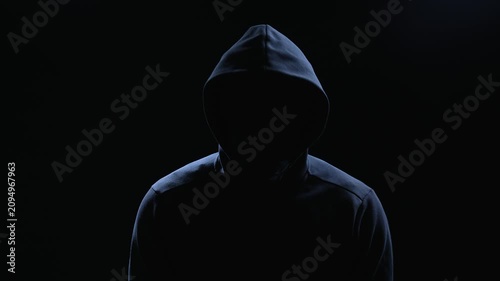 Silhouette of hooded man on black background, threatening villain