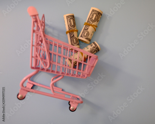 фотографія Small pink toy shopping cart filled with one dollar bills, savings and family budget concept
