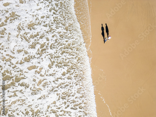Top-Down Drone View of a Couple Walking as a Wave Washes Over the Beach