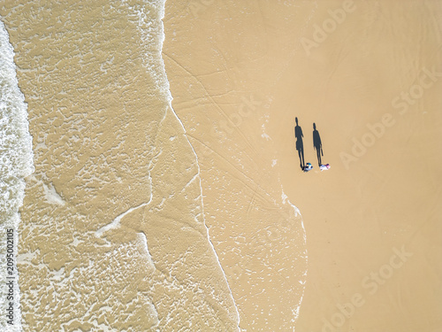 Top-Down Drone View of a Couple Walking as a Wave Washes Over the Beach