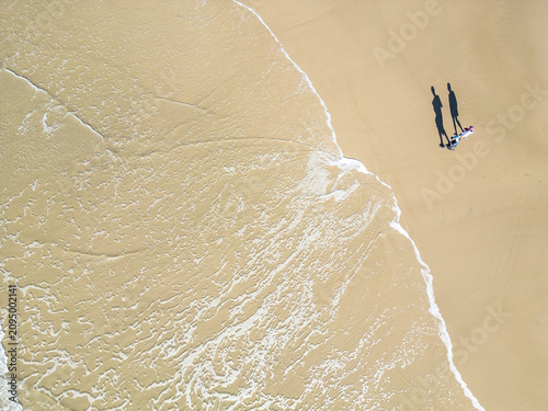 Top-Down Drone View of a Couple Walking as a Wave Washes Over the Beach