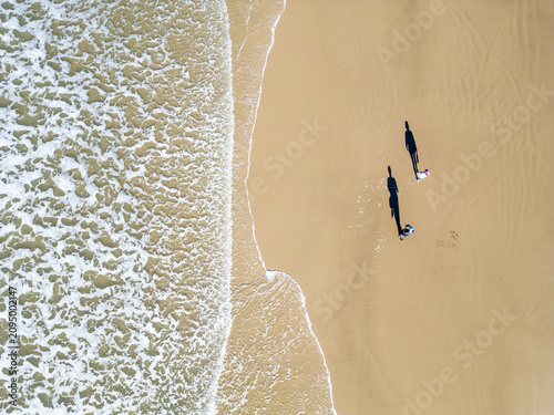Top-Down Drone View of a Couple Walking as a Wave Washes Over the Beach