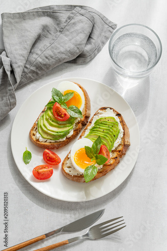 Two avocado toasts with egg, cream cheese, tomatoes, and basil on a concrete background