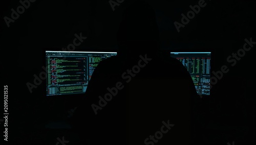 Dark Room With a Person Wearing a Mask Working on a Computer at Night