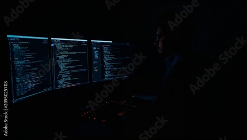 Person Works on Computer in Dim Room With Code Displayed on Screen at Night