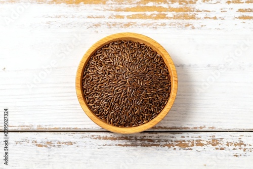 Brown flax seeds in wooden bowl on rustic white wood background