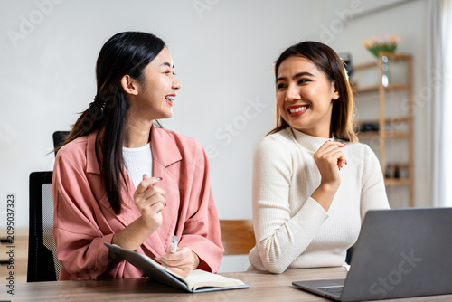 Two women are sitting at a table with a laptop and a notebook