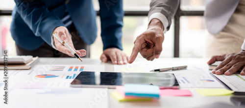 Three people are looking at a table with a lot of papers and a tablet