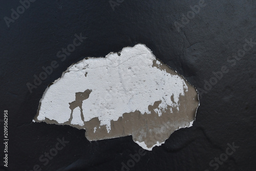 Cracked concrete wall, painted black with a peeling hole