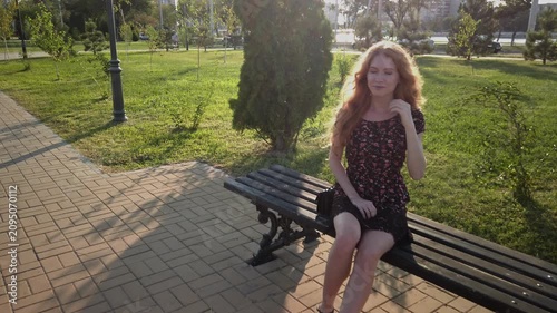 Serene Metropolitan Park Portrait: Young Woman with Copper-Red Hair Enjoying Golden Hour on Wrought-Iron Bench