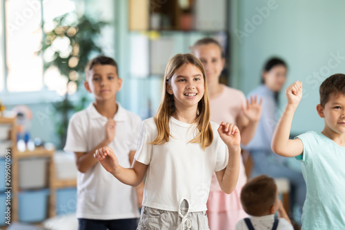 Children actively jump and dance during music lesson, teacher accompanies on piano in kindergarten, music lesson...