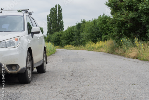 Rural asphalt road in poor condition with damaged pavement and overgrown roadside vegetation. Concept of neglected infrastructure, transportation, and road maintenance.