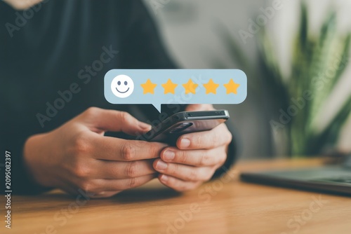 Person holding phone with five-star rating and smiley face on screen at desk