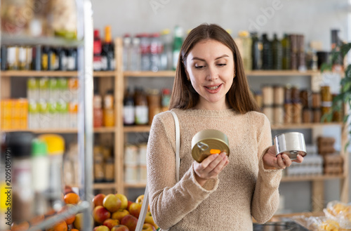 Foto Interested thoughtful young female shopper choosing canned food in local grocery