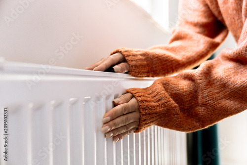 Close-up of a hand adjusting the temperature on a radiator thermostat, regulating home heating for energy efficiency