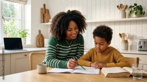 Supportive African American mother helps her young son with school homework in a bright modern kitchen, fostering education and bonding through home learning and focused study sessions at the table!