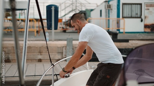 Принти на полотні Man tying a rope on a boat at a marina before setting sail
