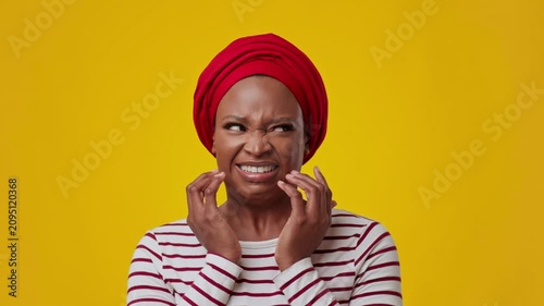 Worried Black Woman In Her 30s Touching Face With Concern At Studio Against Bright Yellow Background, Expressing Distress Or Discomfort. Capturing Emotion In Portrait, Focus On Feelings.
