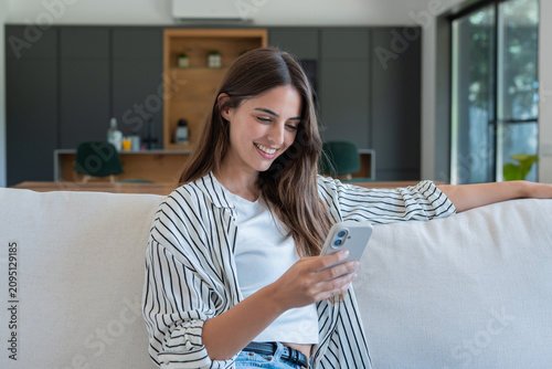 Obraz na płótnie Woman smiling while scrolling mobile phone on a comfortable sofa in a bright mod
