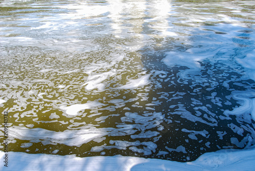 Slika na platnu White foam floating on murky river water surface.