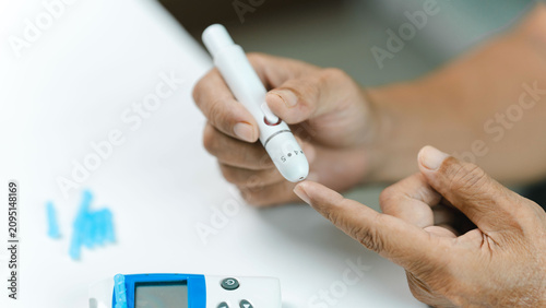 Canvastavla Senior adult performing a finger prick with a lancet device before checking blood glucose using a glucose meter at home