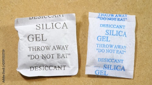 Two white silica gel desiccant packets with printed throw away and do not eat warnings on tan background, close-up video about moisture absorption, packaging safety and accidental ingestion prevention