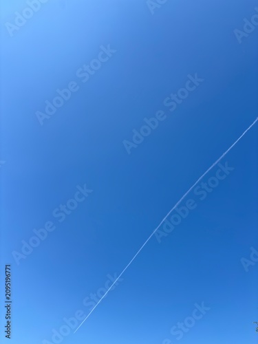 Airplane condensation trail or contrail cutting through a clear blue sky, vertical background