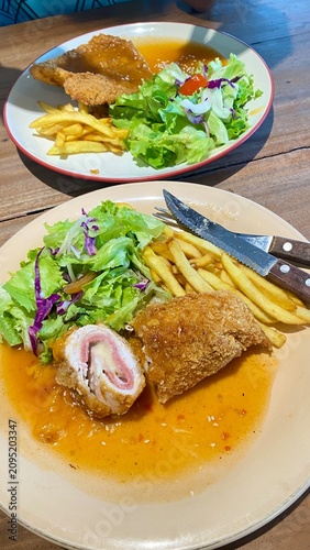 Crispy Breaded Chicken Cordon Bleu Stuffed with Ham and Cheese Served with Fresh Garden Salad and Golden French Fries on a Dining Table