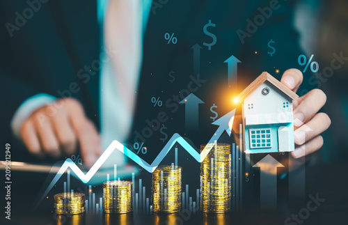Businessman holding home model with growing stacks of gold coins, financial growth chart arrow, percentage icons for real estate investment.