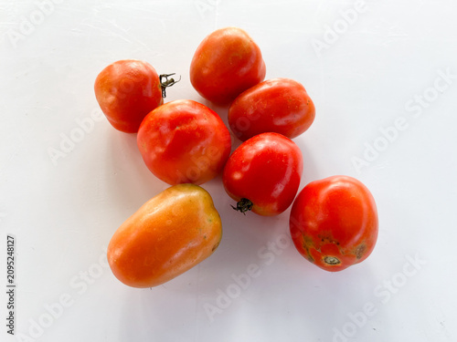 Fotografie Group of ripe red tomatoes with one oblong orange tomato on white background