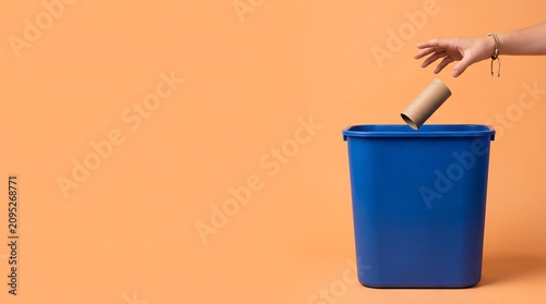 Teenager hand tossing cardboard roll tube into recycling bin on orange background right side empty copy space