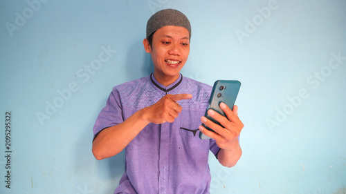 Asian Muslim man holding a cellphone with a happy expression