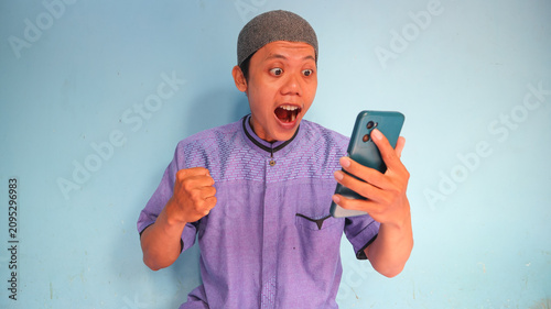 Asian Muslim man holding a cellphone with a happy expression