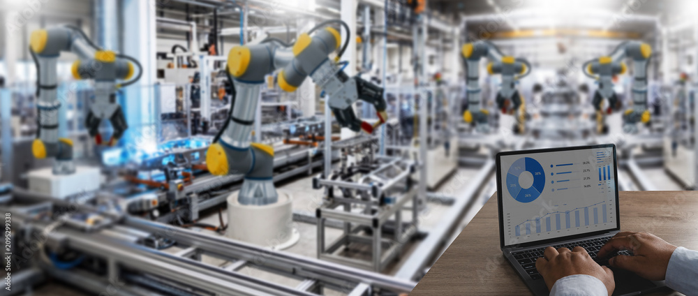 Fototapeta premium Hands type on a laptop dashboard showing industrial data while robotic arms run factory automation for manufacturing control, production monitoring, process analysis, and operations management.