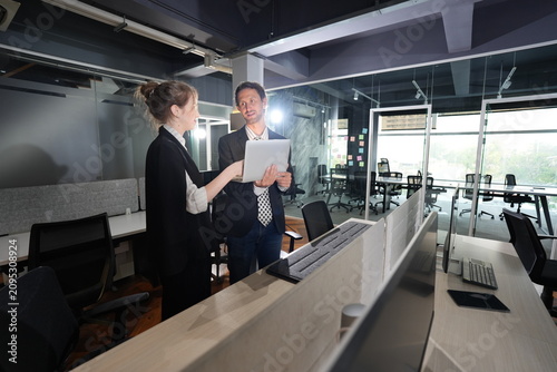 Fotografie Fair-skinned businesswoman touches the laptop screen to highlight a detail as her dark-haired colleague watches, the pair collaborating at a counter in a dim night office