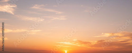 Beautiful sunset sky background with small sun disk on horizon and soft pastel orange pink clouds for panoramic travel mockup design