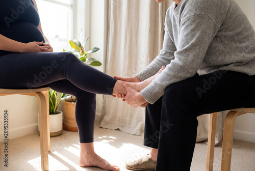 Professional Physiotherapist Performing Ankle Massage For Pregnant Woman At Home