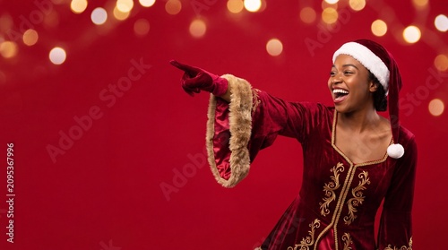 Joyous woman in velvet Santa costume points into negative space.