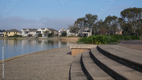 Public waterfront promenade at Sanctuary Lakes against  a row of modern, upscale double-story residential properties in Point Cook, Melbourne Australia. A clean and liveable suburban neigborhood