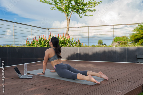 Woman practicing yoga outdoors cobra pose with laptop