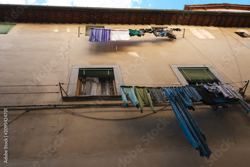 Household laundry hung by local residents dries on outdoor clotheslines strung across the weathered stucco facade of an old historic European apartment building.