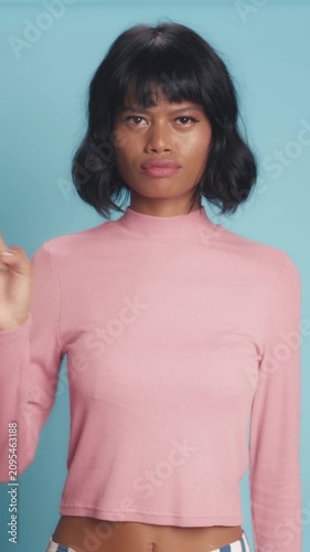 Serious Asian woman with short black hair shakes head side to side and wags index finger in firm disapproval gesture, showing absolute refusal on solid light blue studio background.