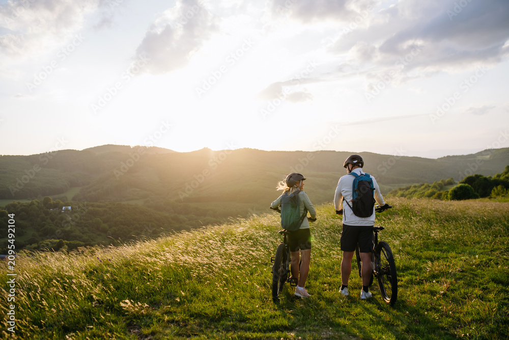 Obraz premium Senior couple taking break during e-bike ride, looking at sunset.