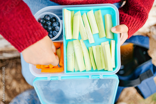 Close up of child hand taking carrot stick from healthy lunch box