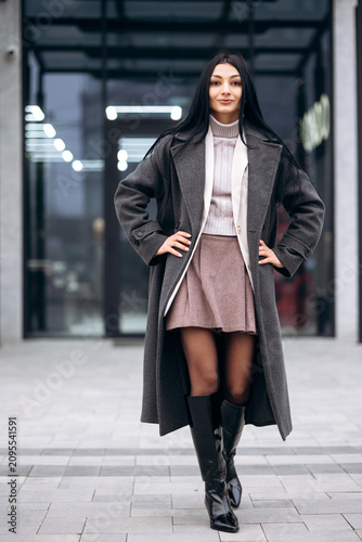 Confident woman modeling a new winter coat and boots in an urban street setting. She is looking at the camera