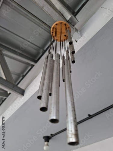 Foto bottom-up perspective of a metallic wind chime made of several silver aluminum tubes hanging from a round wooden base underneath a corrugated ceiling