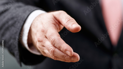 A photograph showing an outstretched right hand of a person in business attire, ready for a handshake. the hand is angled downwards with fingers relaxed and slightly bent. Ai generated
