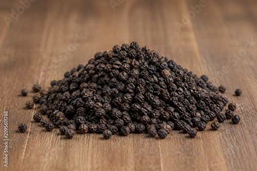 Heap of black peppercorns arranged on wooden tabletop surface