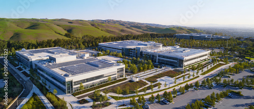 Ultra realistic aerial commercial photography, contemporary enterprise data center campus surrounded by landscaped green areas and rooftop solar panels, balanced architecture