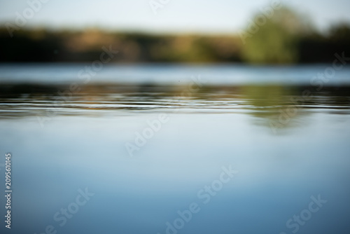 Low angle macro shot of calm water surface ripples on a river with a heavily blurred bokeh background of a shore